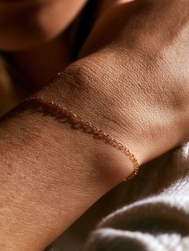 A white model wearing a thin gold bracelet on...